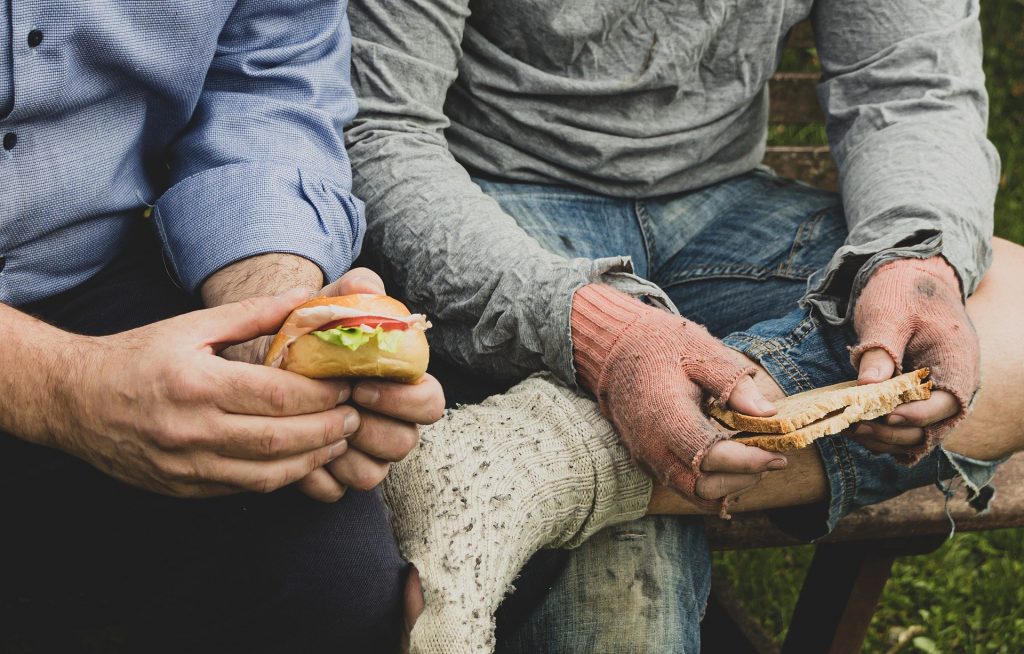 photo of homeless man eating with a person supporting them