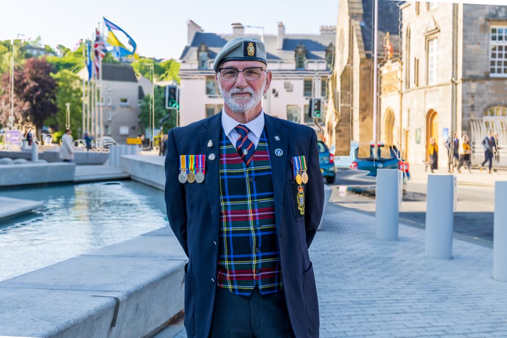 Scottish male veteran standing in uniform and smiling at the camera